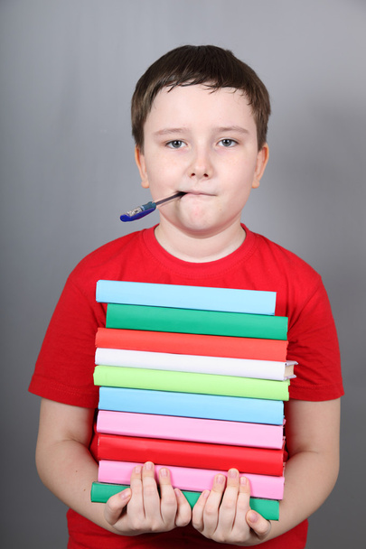 Boy with a pen in his mouth holding a stack of books - Photo, Image