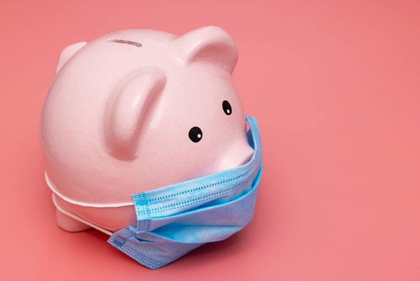 Concept of economic crisis. Piggy bank with protective mask on pink background. - Photo, Image