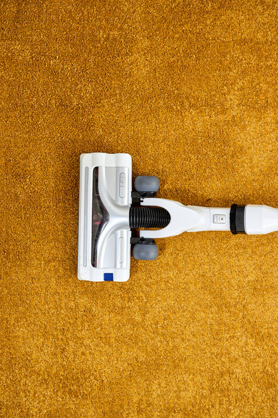 Close-up photo of vacuum cleaner applied on yellow carpet at home removing dust - Photo, Image