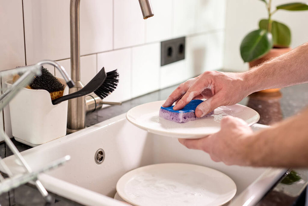 Cropped male hands washing dishes at kitchen sink while doing cleaning at home at weekends - Φωτογραφία, εικόνα