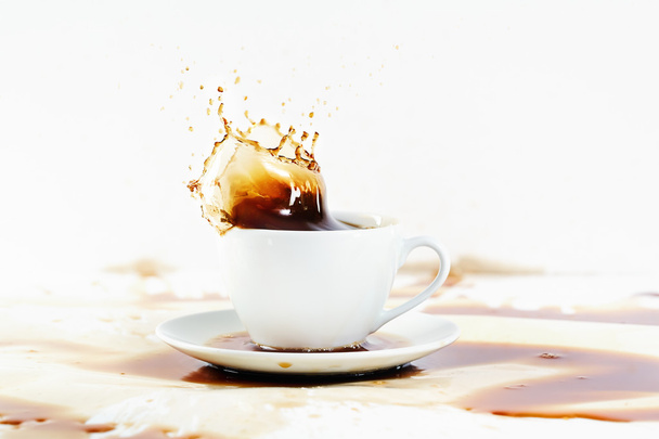 Cup of coffee creating splash. White background, coffee stains. - Фото, изображение
