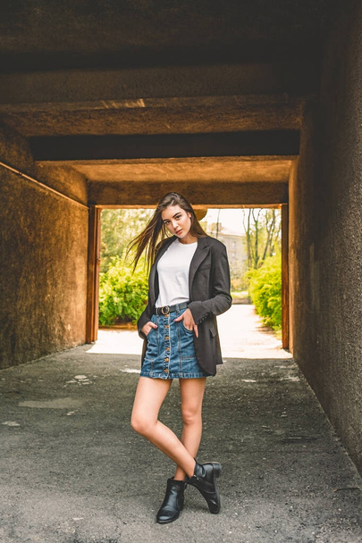 Girl in a denim skirt on the street in the spring. girl fashion style model. The girl in the arch. - Photo, Image