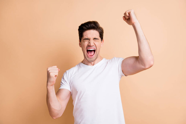Photo of cheerful young man closed eyes raise fists celebrate victory isolated on pastel beige color background - Fotografie, Obrázek