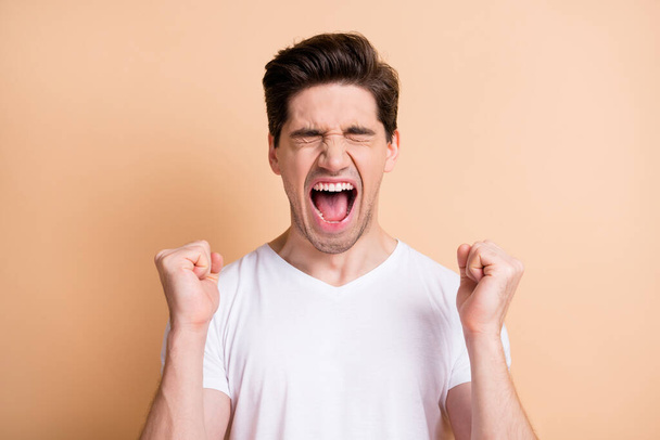 Portrait of hooray brunet man yell hands fists wear white t-shirt isolated on beige color background - Φωτογραφία, εικόνα