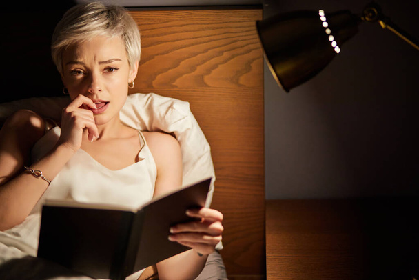 Female is passionate about reading book and worries about heroes, alone at home at night - Foto, Bild