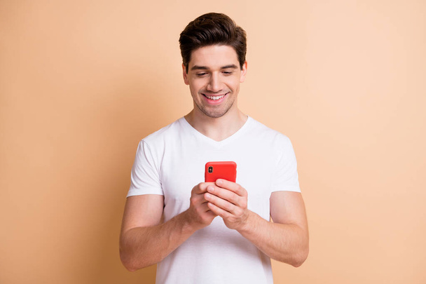 Photo of handsome young person hold phone look screen toothy smile isolated on beige color background - Foto, imagen