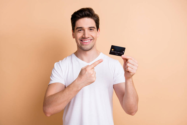 Portrait of handsome positive cheerful person indicate finger debit card isolated on beige color background - Foto, imagen