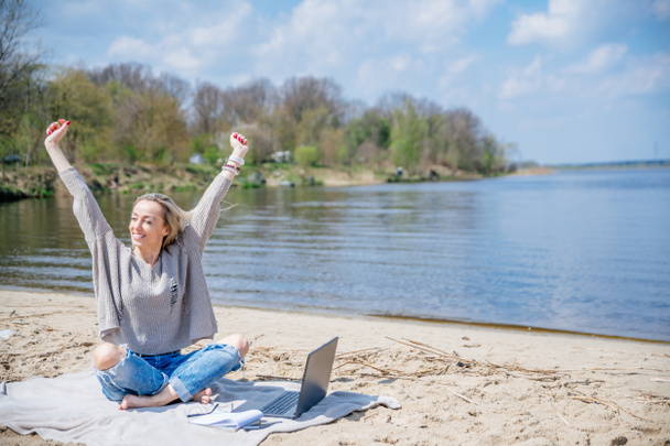 Podekscytowana kobieta, kobieta freelancer z laptopem trzymając ręce w górze podczas pracy zdalnie podczas wakacji letnich. - Zdjęcie, obraz