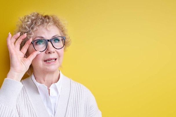 Surprised impressionable senior woman looking at side fixing eyeglasses - Photo, image
