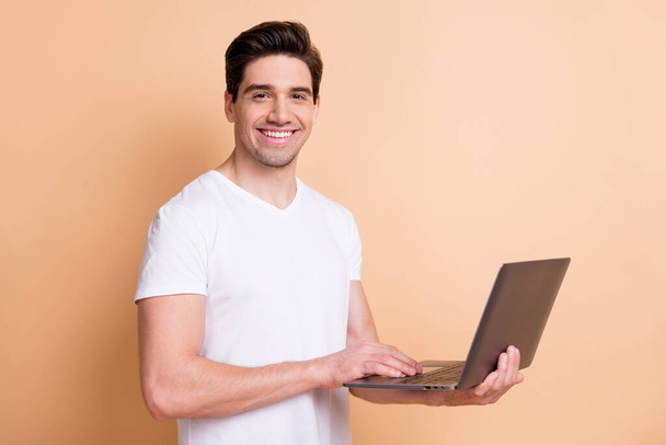 Photo of satisfied young person toothy smile writing text on computer isolated on beige color background - Photo, image