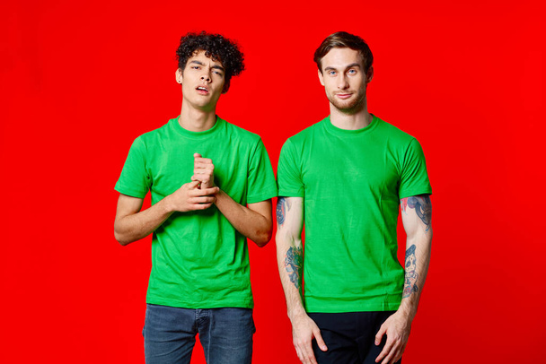 Yeşil tişörtlü iki neşeli arkadaş iletişim mutluluğu kırmızı arka plan - Fotoğraf, Görsel