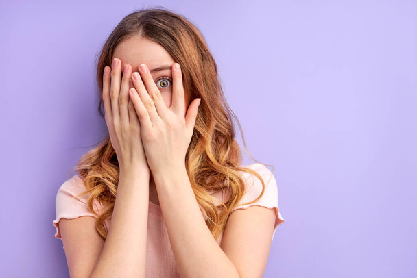 beautiful young pretty scared woman posing isolated over purple background covering face - 写真・画像