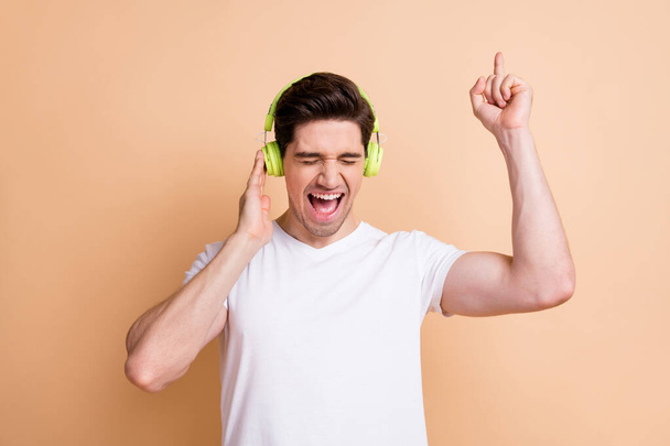 Photo of cheerful person closed eyes touch headphones finger direct up favorite single isolated on beige color background - Фото, изображение