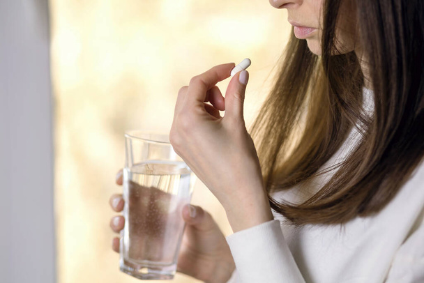 Naisella on lasi vettä ja pilleri käsissään. Potilas hoitaa tautia antibiooteilla. Päänsärkyä tai vatsakipua voidaan lievittää lääkkeillä ja kipulääkkeillä - Valokuva, kuva