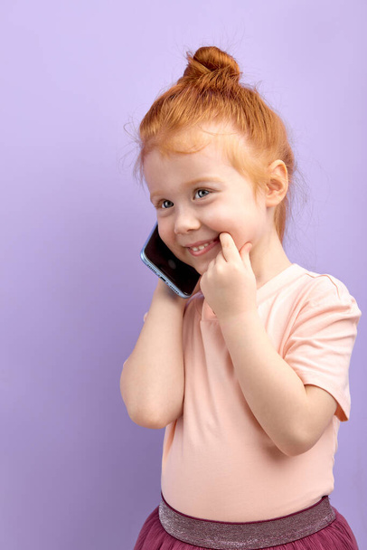 Cute child holding cell phone, smiling, having nice talk with someone - Foto, Imagen
