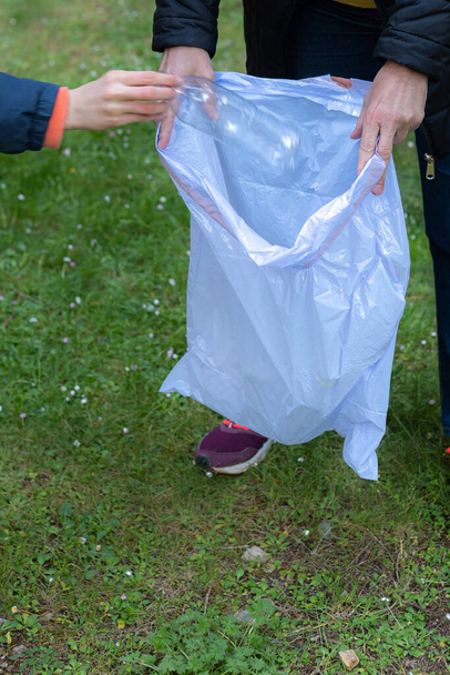 Λεπτομέρεια ανακύκλωσης πλαστικής φιάλης που τοποθετείται σε σακούλα σκουπιδιών στη μέση του θάμνου από δύο εθελοντές με επιλεκτική εστίαση έννοια φροντίδα της φύσης και την ανακύκλωση - Φωτογραφία, εικόνα