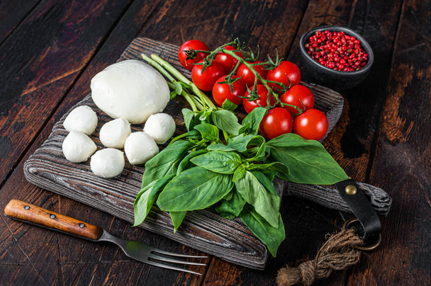 Mozzarella kaas, basilicum en tomatenkers op houten plank, Ingrediënten voor Caprese salade. Donker houten achtergrond. Bovenaanzicht - Foto, afbeelding