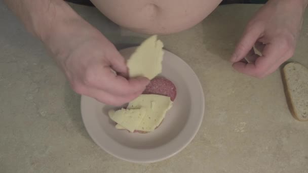 A kövér ember csinál egy szendvicset sajttal, kolbásszal és megtölti majonézzel, ketchuppal. - Felvétel, videó