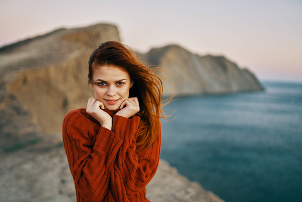 happy woman in a red sweater in the mountains in nature and the sea in the background - Photo, Image