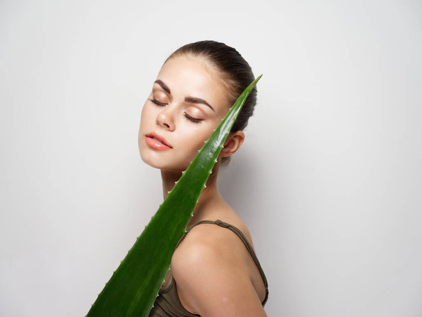 beautiful woman with aloe leaf near face on light background cropped view  - Photo, image