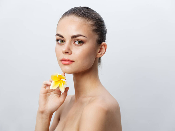 beautiful woman holding a yellow flower in her hands on a light background  - Photo, Image