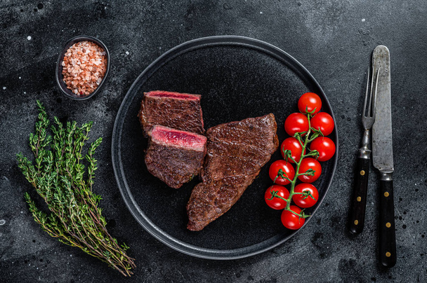 Gebratenes Steak vom Denver-Rindfleisch auf einem Teller mit Thymian. Schwarzer Hintergrund. Ansicht von oben - Foto, Bild