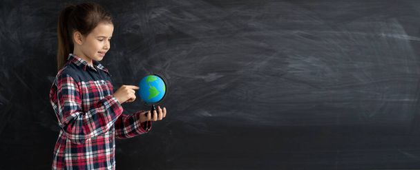 young caucasian girl schoolgirl or student stands near the chalk blackboard. Holds a globe. Baner - Photo, Image