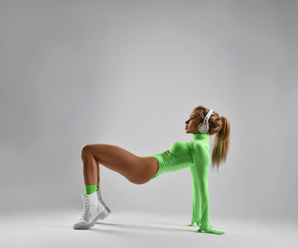 Sexy blonde woman, sporty girl in stylish sportswear jumpsuit and brutal shoes does pelvic lifts, standing on tiptoe - Foto, Imagem