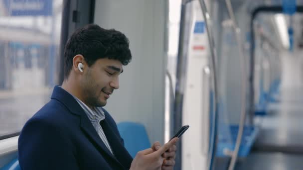 Side view of man in wireless earphones using mobile in metro - Кадри, відео