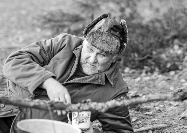 Schwarz-Weiß-Foto eines Försters am Feuer, Mann trinkt Tee, verschwommener Waldhintergrund, wild - Foto, Bild