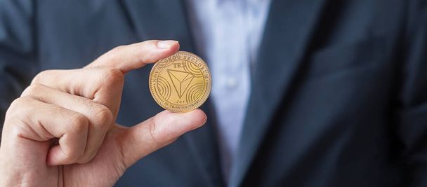 man hand houden goud Tron munt (TRX) cryptogeld, Crypto is digitaal geld binnen de blockchain netwerk, wordt uitgewisseld met behulp van technologie en online uitwisseling. Gedecentraliseerd financieel concept - Foto, afbeelding