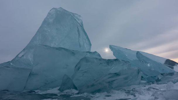 Un bloque de grandes hummocas de hielo sobre el fondo de un cielo nublado. Los témpanos de hielo turquesa transparentes están en posición vertical. El sol es visible en la brecha. - Foto, imagen