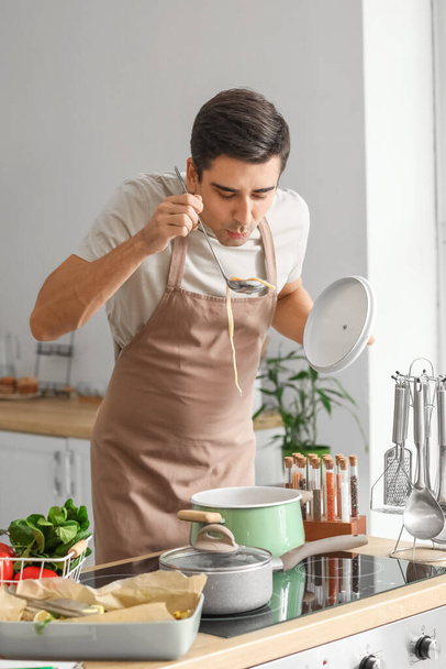 Junger Mann verkostet Gericht in Küche - Foto, Bild