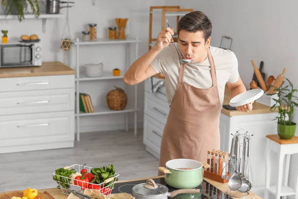 Молодий чоловік дегустує страву на кухні
 - Фото, зображення