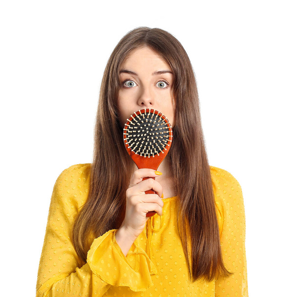 Überraschte junge Frau mit Haarbürste auf weißem Hintergrund - Foto, Bild