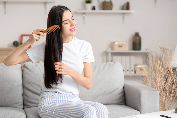 Beautiful young woman combing hair at home - Foto, afbeelding