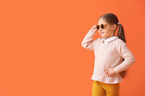 Schattig klein meisje dragen stijlvolle zonnebril op kleur achtergrond - Foto, afbeelding