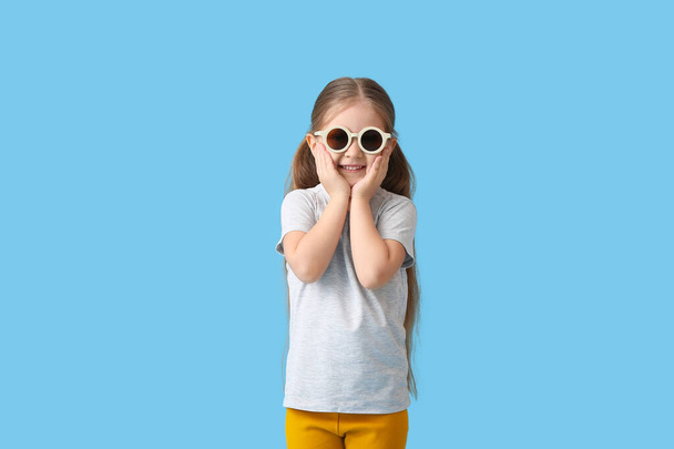 Cute little girl wearing stylish sunglasses on color background - Foto, imagen
