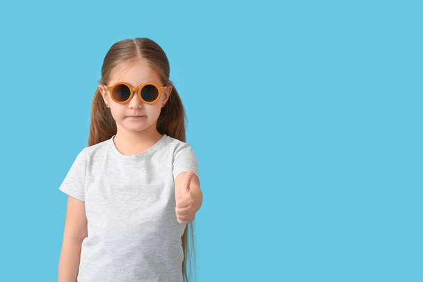 schattig klein meisje dragen stijlvolle zonnebril en tonen duim-up op kleur achtergrond - Foto, afbeelding