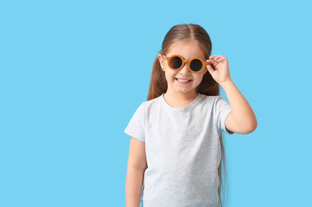 Menina bonito vestindo óculos de sol elegantes no fundo de cor - Foto, Imagem