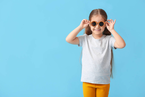 Cute little girl wearing stylish sunglasses on color background - Fotó, kép