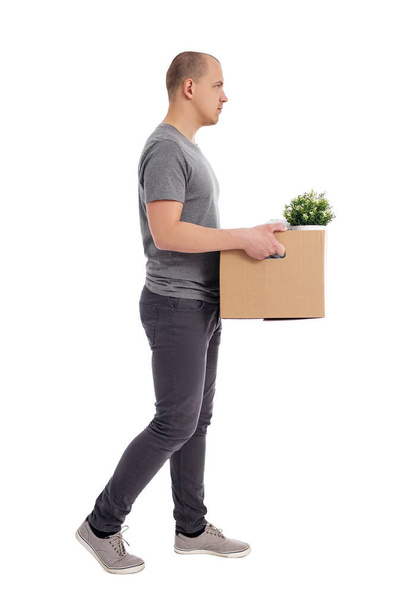 side view of young handsome walking man holding box with belongings isolated on white background - Fotó, kép