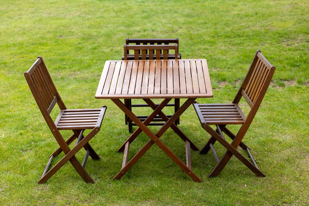 деревянный стол и стулья на газоне в саду  - Фото, изображение