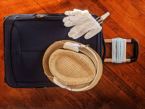 Travel preparations after the end of quarantine. New life after pandemic and prevent coronavirus (COVID-19) concept. Medical face masks, gloves, sanitizer, sunglasses and beach hat on baggage close up - Photo, Image