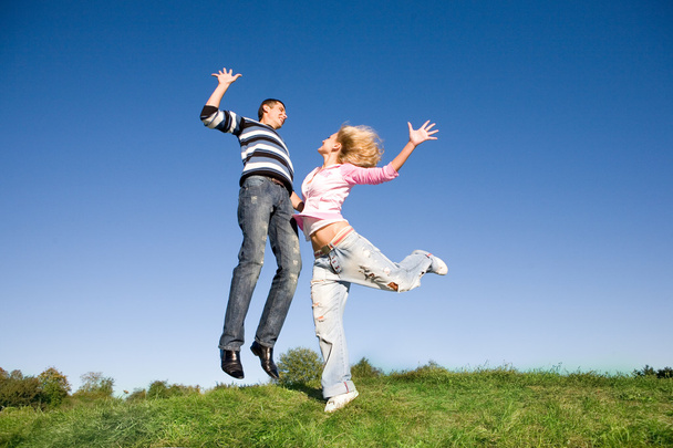 Happy young couple jumping in sky above a green meadow - Photo, Image