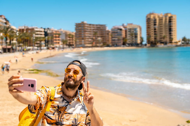 A young tourist taking a selfie at Playa del Cura in the coastal city of Torrevieja, Alicante, Valencian Community. Spain, Mediterranean Sea - Valokuva, kuva