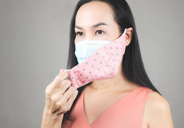 Nahaufnahme von asiatischen Frau trägt rosa gepunktete Tuchmaske auf medizinische Gesichtsmaske für besseren Schutz vor covid-19 Ausbruch. Double Gesichtsmasken für covid19 Schutz. - Foto, Bild