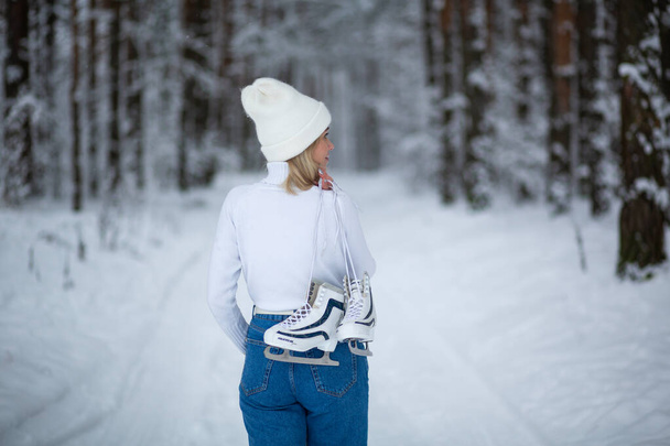 Jeune blonde belle femelle avec des patins à glace blancs à la main en hiver forêt enneigée.  - Photo, image