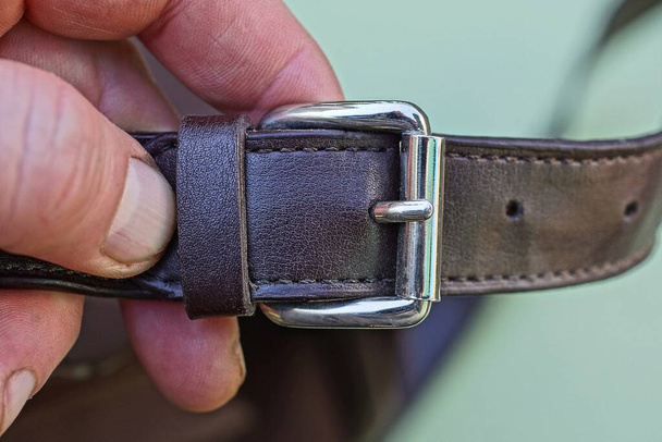 a brown leather harness with a gray metal fastener hold on the fingers on a green background - Foto, Imagen