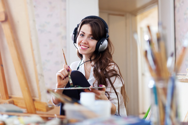 Female artist in headphones paints picture  - Фото, изображение
